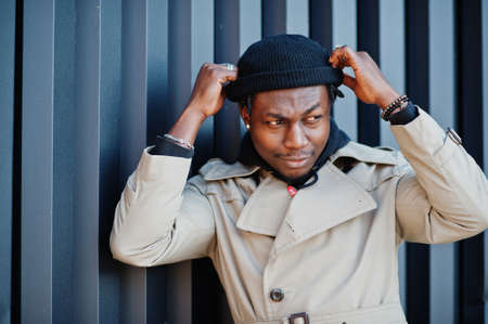 Handsome african american man posing outside in black hat and beige coat.