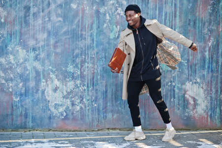 Handsome african american man posing outside in black hat and beige coat with folder in hand.