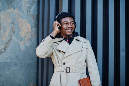 African american man with headphones, wear on hat and coat listening music on steel background.