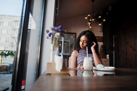 Ð¡harming elegant young african american woman with long curly hair wearing jumpsuit sitting at cafe indoor.の写真素材