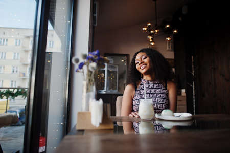 Ð¡harming elegant young african american woman with long curly hair wearing jumpsuit sitting at cafe indoor.の写真素材