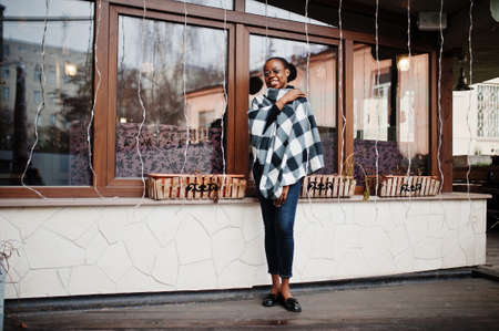 African woman in checkered cape and eyeglasses posed outdoor.