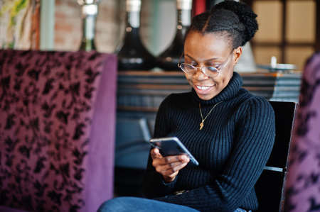 African woman in black sweater sitting at cafe and look at mobile phone.の写真素材