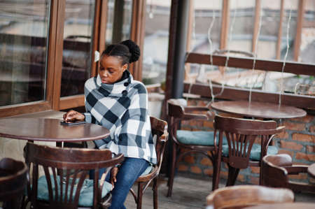 African woman in checkered cape posed outdoor cafe terrace with mobile phone.の写真素材