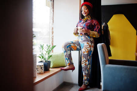 Enthusiastic african american woman in trendy colored outfit with red beret chilling in cozy cafe...