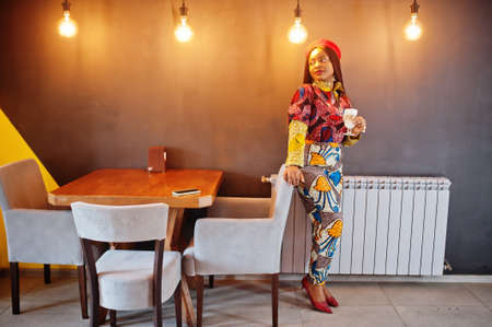 Enthusiastic african american woman in trendy colored outfit with red beret chilling in cozy cafe...