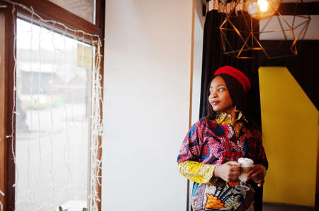 Enthusiastic african american woman in trendy colored outfit with red beret chilling in cozy cafe...