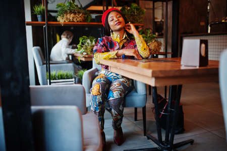 Enthusiastic african american woman in trendy colored outfit with red beret chilling in cozy cafe.