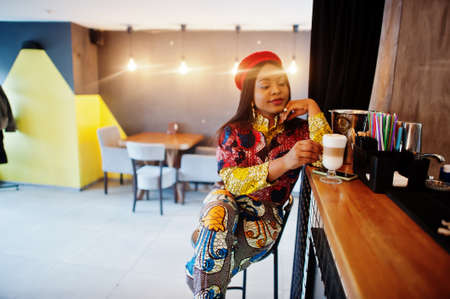 Enthusiastic african american woman in trendy colored outfit with red beret chilling in cozy cafe,...