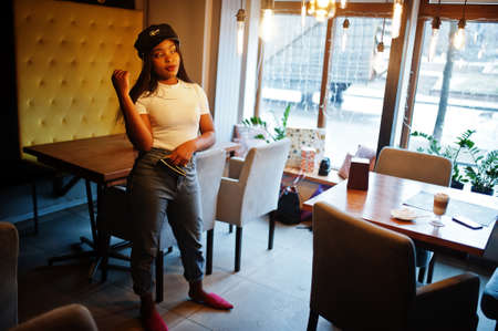 Fashionable african american woman in black cap chilling in cozy cafe.の写真素材