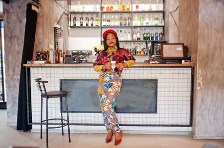 Enthusiastic african american woman in trendy colored outfit with red beret chilling in cozy cafe,...