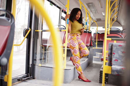 Young stylish african american woman riding on a bus with mobile phone.