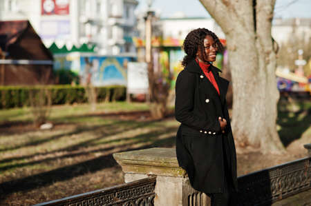 Portrait of a curly haired african woman wearing fashionable black coat and red turtleneck posing...