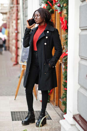 Portrait of a curly haired african woman wearing fashionable black coat and red turtleneck posing...