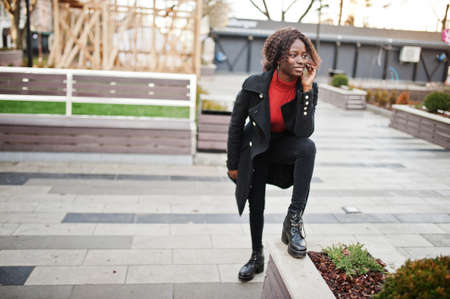 Portrait of a curly haired african woman wearing fashionable black coat and red turtleneck posing...