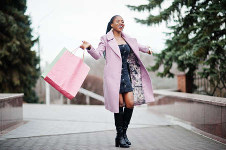 Young stylish beautiful african american woman in street, wearing fashion outfit coat with shopping bags and mobile phone at hands.の写真素材