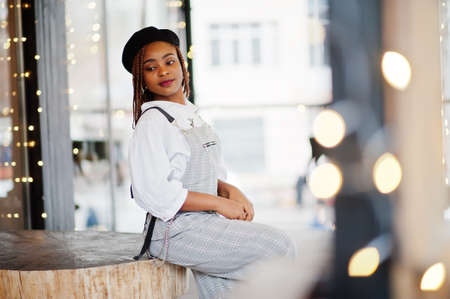 African american woman in overalls and beret posed in outdoor terrace with christmas decorations garland.の写真素材