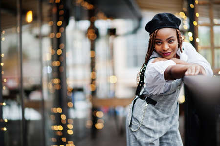 African american woman in overalls and beret posed in outdoor terrace with christmas decorations garland.の写真素材