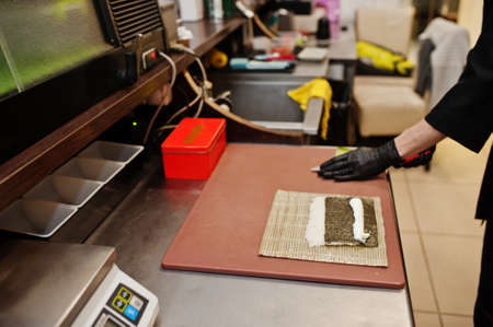 Close up hands of professional chef wear in black gloves making sushi and rolls in a restaurant...