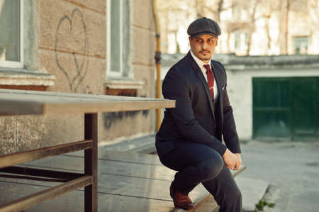 Portrait of retro 1920s english arabian business man wearing dark suit, tie and flat cap.