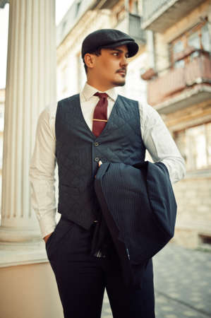 Portrait of retro 1920s english arabian business man wearing dark suit, tie and flat cap.