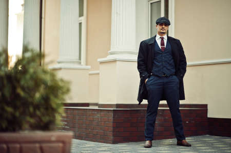 Portrait of retro 1920s english arabian business man wearing dark coat, suit, tie and flat cap.