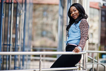 Hipster african american girl wearing jeans shirt with leopard sleeves posing at street against...