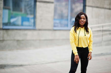 Hipster african american girl wearing yellow hoodie posing at street.