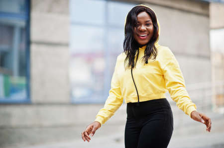 Hipster african american girl wearing yellow hoodie posing at street.