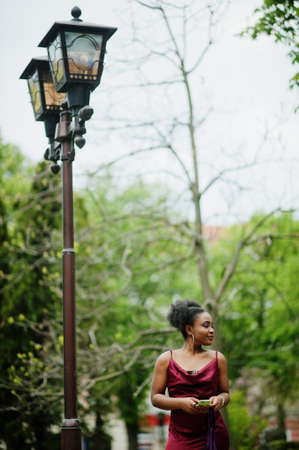Portrait of a beautiful natural young African woman with afro hair. Black model in red silk dress with mobile phone.の写真素材
