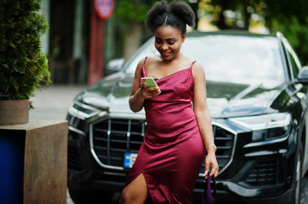 Portrait of a beautiful natural young African woman with afro hair. Black model in red silk dress with mobile phone.の写真素材