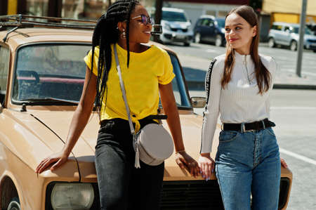 White caucasian girl and black African American together against old retro car. World unity, racial...