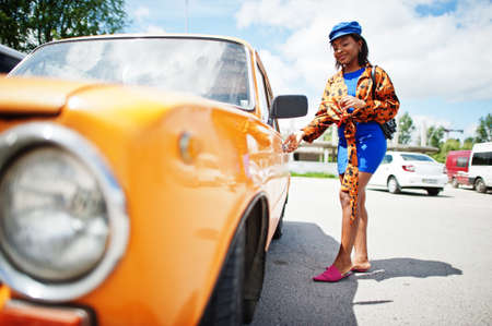 Beautiful african american lady with sunglasses standing near orange classic retro car.