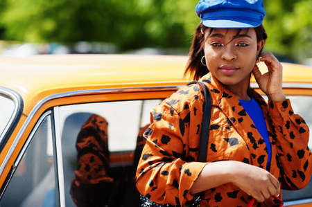 Beautiful african american lady standing near orange classic retro car.の写真素材