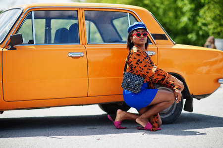 Beautiful african american lady with sunglasses standing near orange classic retro car.の写真素材