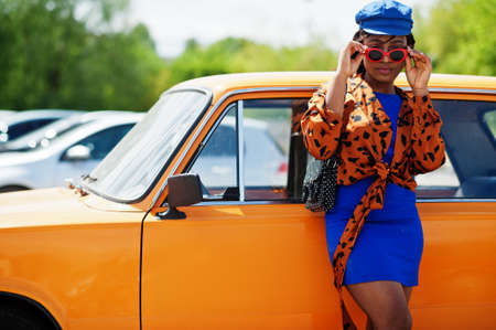 Beautiful african american lady with sunglasses standing near orange classic retro car.の写真素材