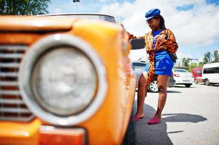 Beautiful african american lady with sunglasses standing near orange classic retro car.の写真素材