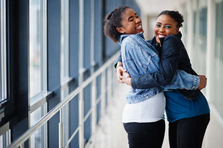 Two african woman friends in jeans jacket hugging indoor together.の写真素材
