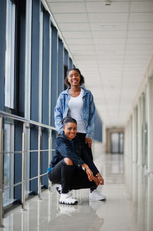 Two african woman friends in jeans jacket posed indoor together.