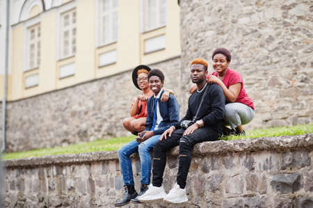 Four african friends having fun outdoors. Two black girls with guys sit an old city.の写真素材
