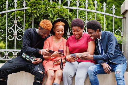 Four african friends having fun outdoors. Two black girls with guys with mobile phones.の写真素材