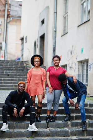 Four african friends having fun outdoors. Two black girls with guys sit on stairs of an old city.の写真素材