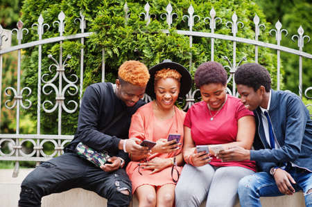 Four african friends having fun outdoors. Two black girls with guys with mobile phones.の写真素材