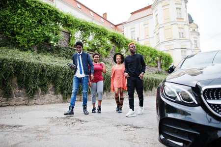 Four african friends walking near luxury car outdoors. Two black girls with guys.の写真素材