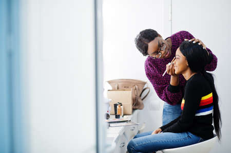 African American woman applying make-up by make-up artist at beauty saloon.の写真素材