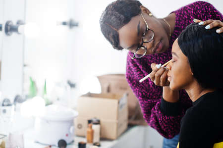 African American woman applying make-up by make-up artist at beauty saloon.の写真素材