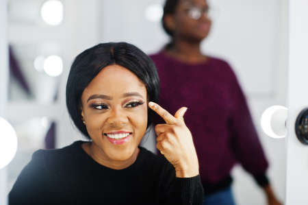 African American woman applying make-up by make-up artist at beauty saloon.