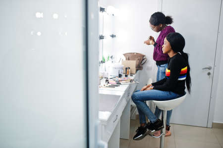 African American woman applying make-up by make-up artist at beauty saloon.