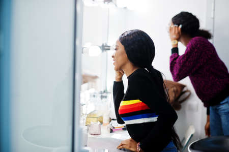 African American woman applying make-up by make-up artist at beauty saloon.