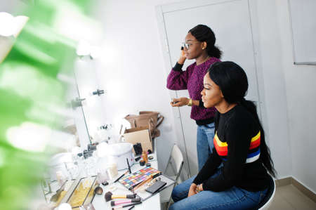 African American woman applying make-up by make-up artist at beauty saloon.の写真素材